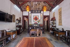 Una habitación tradicional china con suelo de madera, un televisor montado en la pared y una gran mesa de madera en el centro.