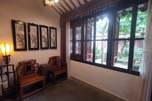 Una habitación tradicional con muebles de madera, un ventanal con diseño de celosía y obras de arte enmarcadas en la pared.