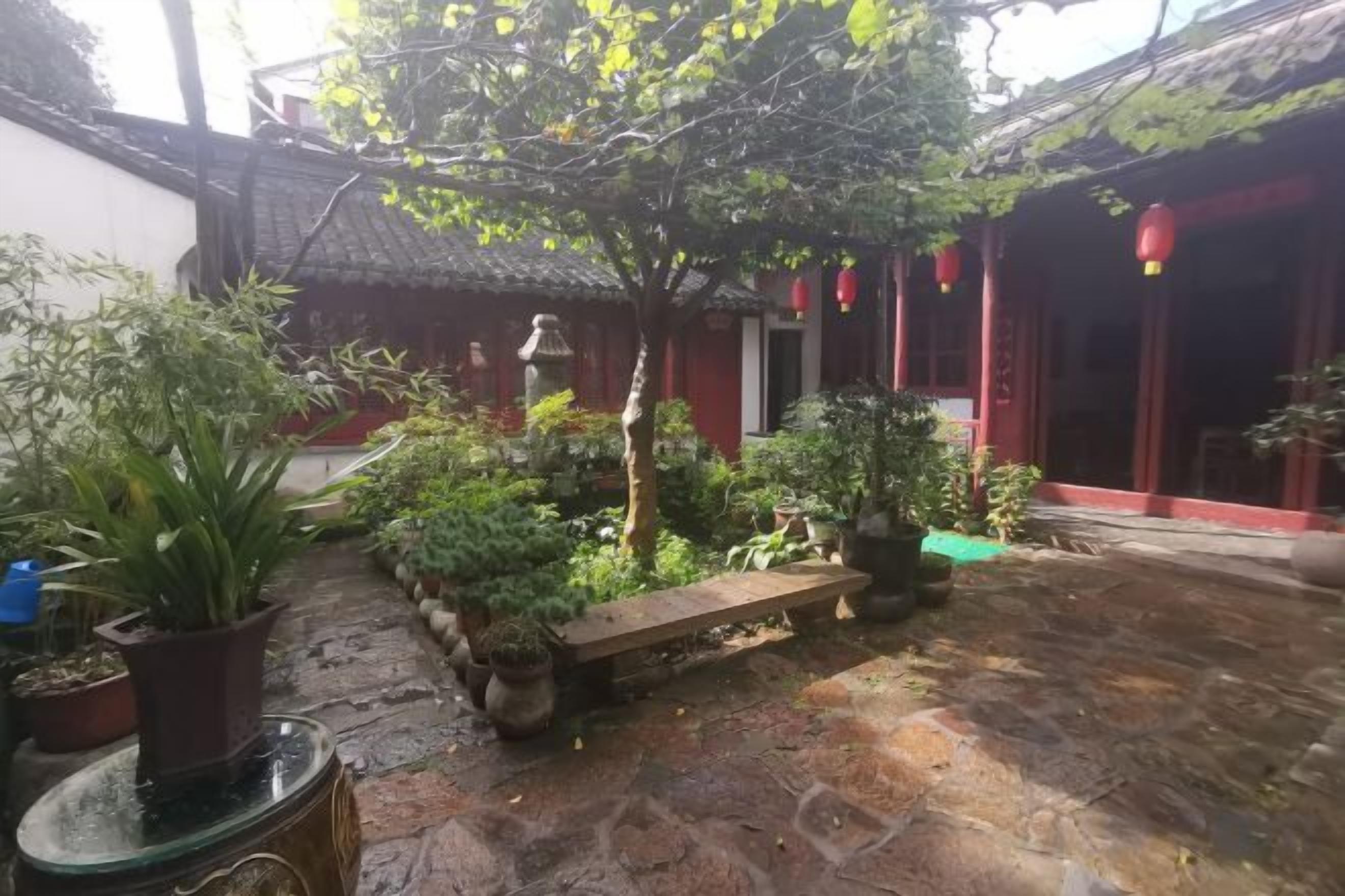 Une cour dallée de pierres, agrémentée de plantes en pot, d’un banc et présentant une architecture traditionnelle.