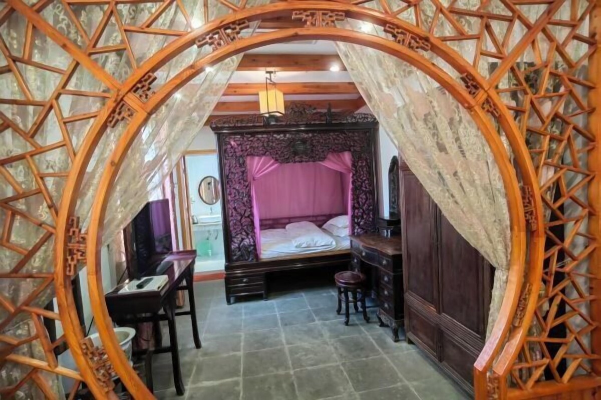 A traditional room with a four-poster bed, a desk, and a chair.