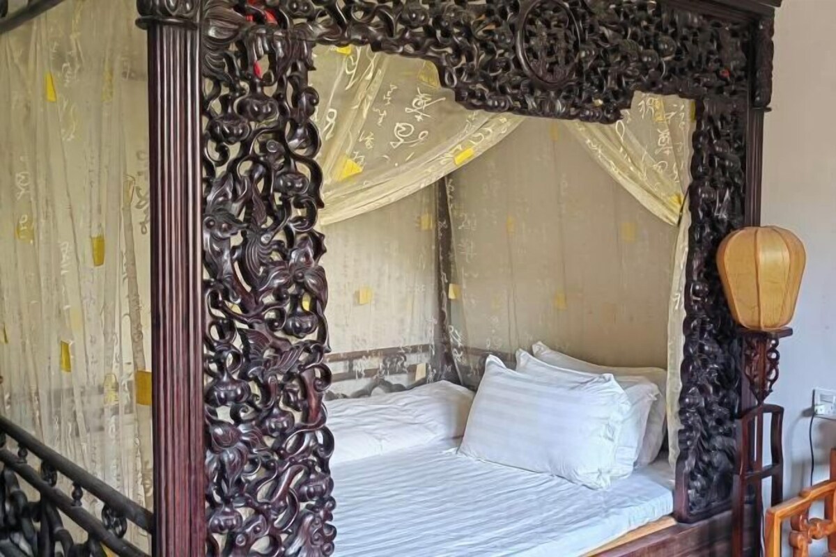 A four-poster bed with ornate carvings, a canopy, and a traditional wooden headboard.