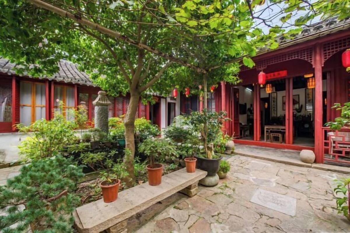 A traditional courtyard with stone flooring, potted plants, and red-framed buildings.