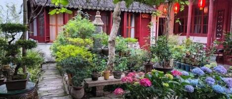 Un patio tradicional con plantas en macetas, un camino de piedra y edificios de color rojo con tejados de tejas.