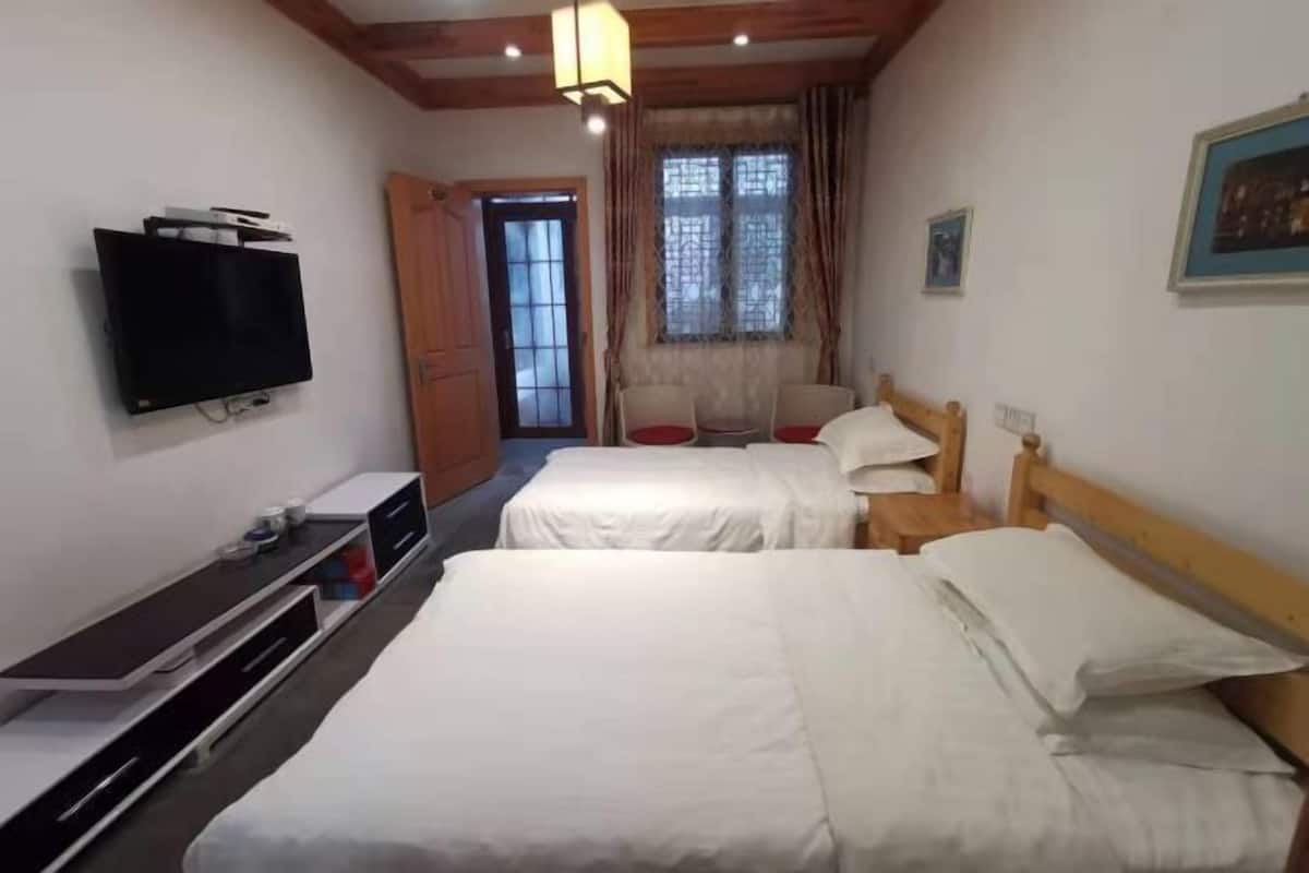 A hotel room with two beds, a TV, a desk, and a window with curtains.