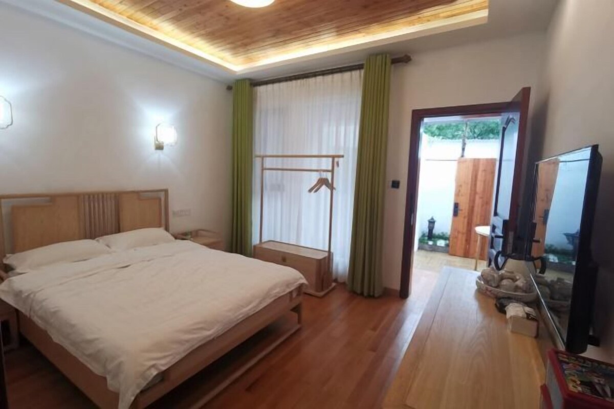 A bedroom with a wooden bed, a bedside table, a hanging rack, and a television.