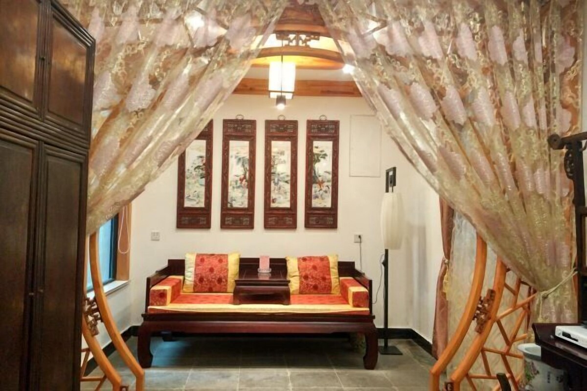A traditional room with a wooden sofa, a ceiling fan, and a wall-mounted TV.