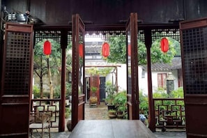 A traditional wooden room with a table and chairs, a view through an open door, and red lanterns.