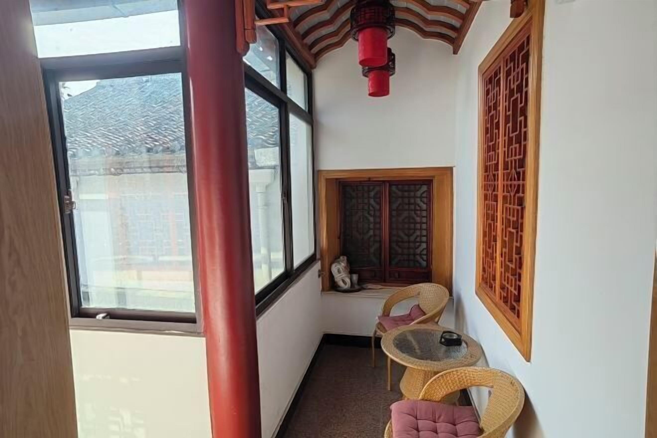 A narrow corridor with a large window, a small table with chairs, and traditional wooden lattice windows.