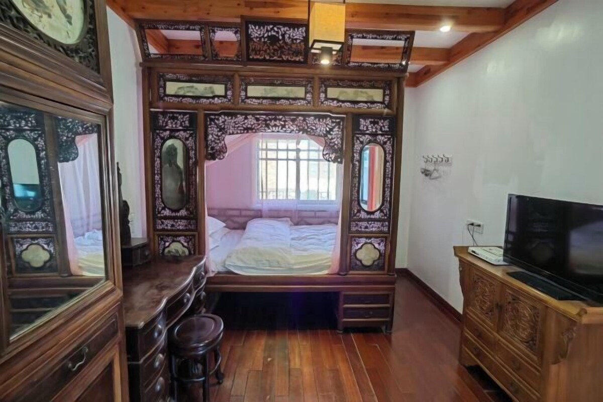 A bedroom with a wooden bed frame, a television, and a dresser.