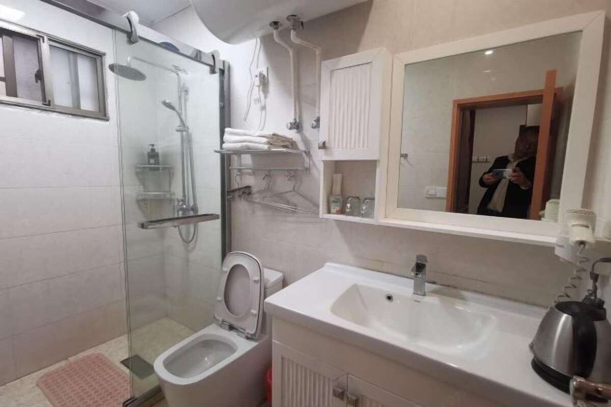 A modern bathroom with a glass-enclosed shower, a toilet, a sink, and a mirror.