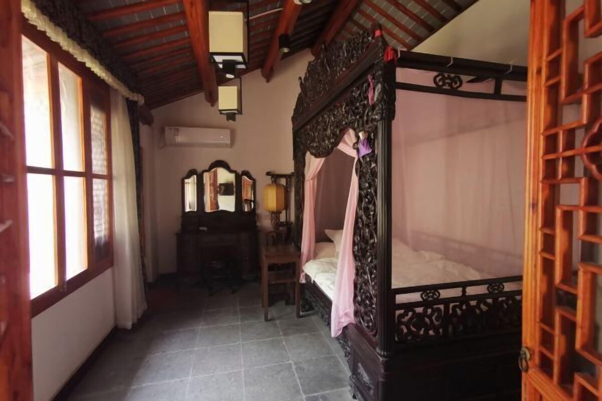 A traditional room with a four-poster bed, a wooden cabinet, and a mirror.