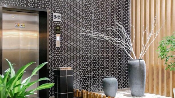 Eine moderne Lobby mit Wand in sechseckigem Muster, einer Wand mit Holzleisten auf der rechten Seite, einer großen grauen Vase und einem Empfangstresen.