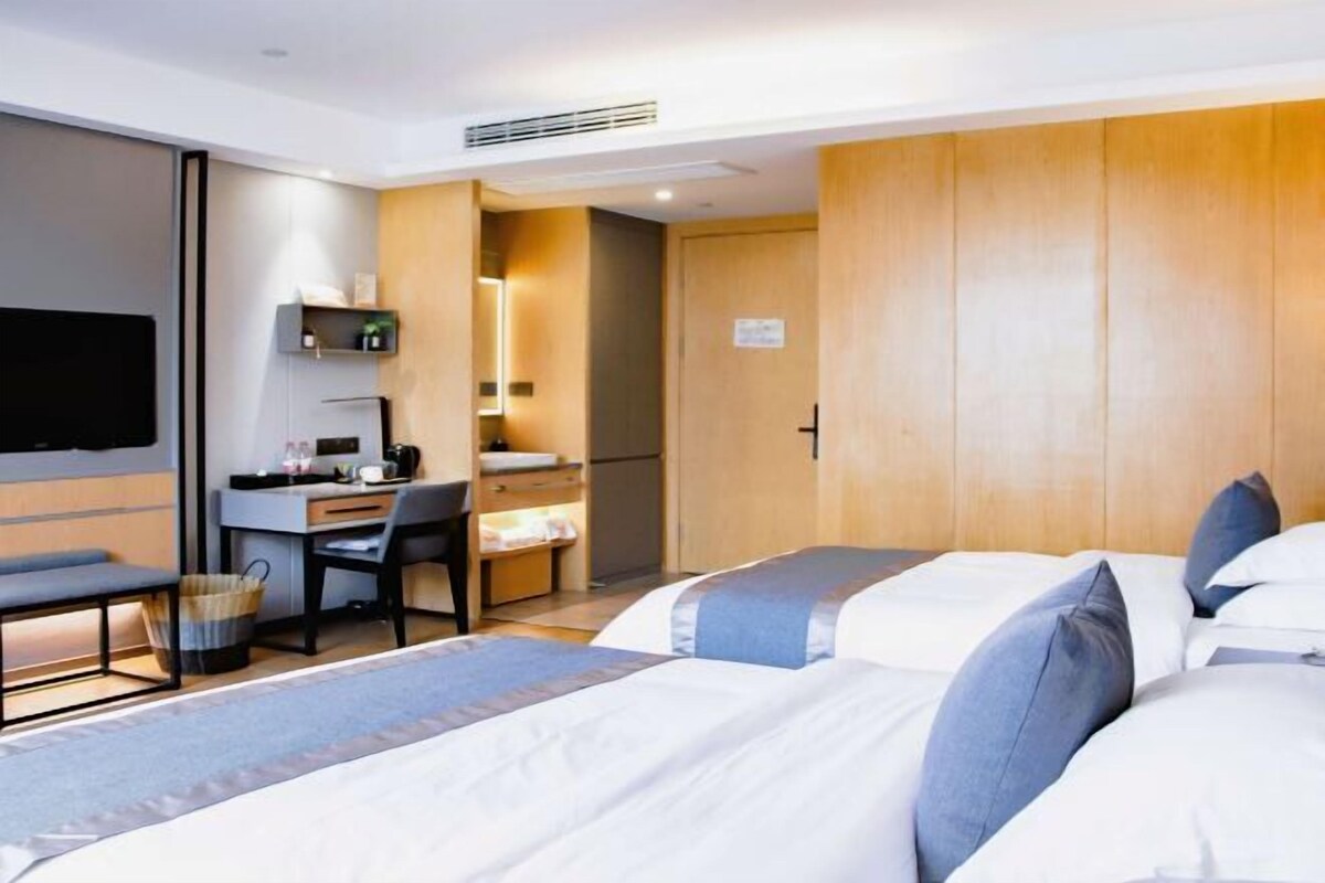 A hotel room with two beds, a desk, a chair, a TV, and a wardrobe.