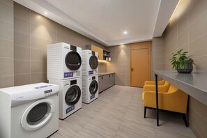 A laundry area with stacked washing machines, a small kitchenette, and a seating area with a chair. - Free Living Hotel (Daishan)