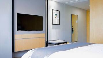 A modern hotel room with a bed, a mounted TV, a framed picture on the wall, and a door with a mirror.