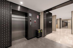 A modern elevator with a metallic finish, a wall with a geometric pattern, and a sign indicating a coffee area. - Free Living Hotel (Daishan)
