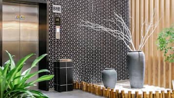 An elevator with a metallic finish, a wall with a geometric pattern, and a large grey vase with branches.