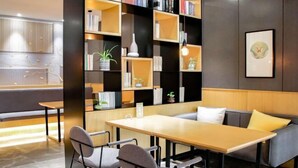 Ein modernes Interieur mit einem Holztisch und Stühlen, einem Sofa und einem Bücherregal, das mit Büchern und Dekoration gefüllt ist.