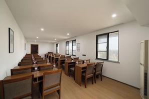 A conference room with rows of tables and chairs, large windows, and a door in the background. - Free Living Hotel (Daishan)
