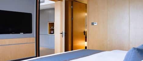 Habitación de hotel moderna con una cama grande, un armario de madera y un televisor montado en la pared.