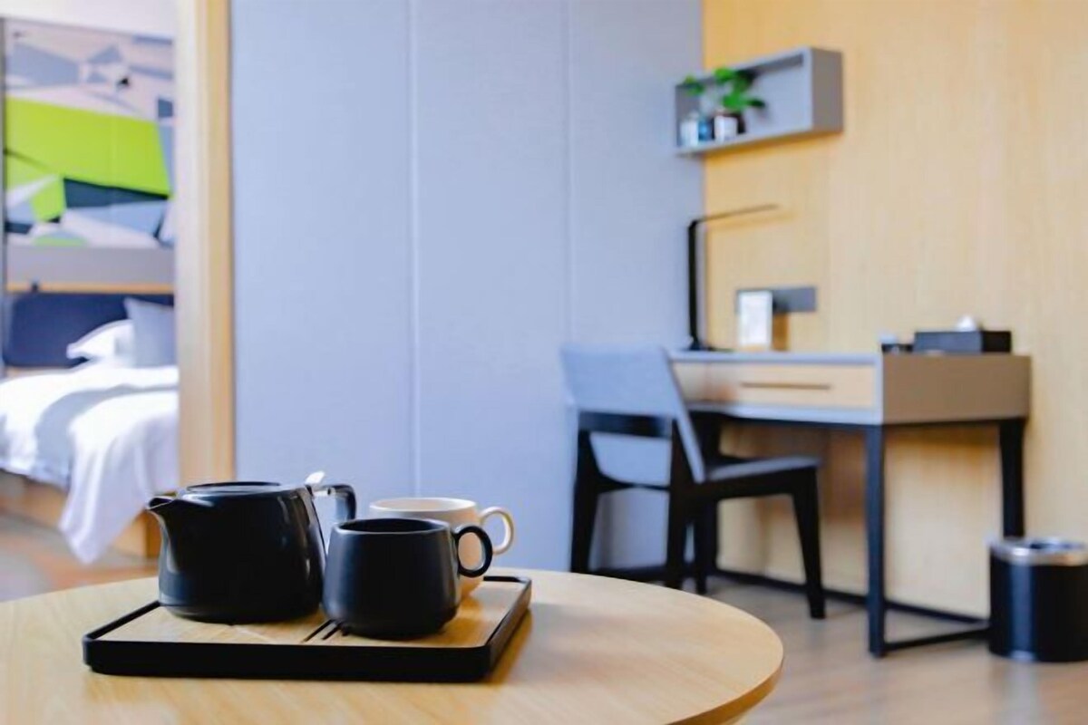 A hotel room with a bed, a desk, and a coffee table with a black mug and a teapot.