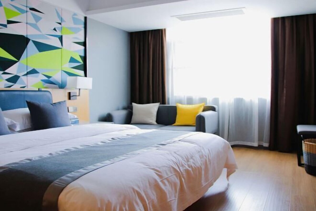 A hotel room with a large bed, a sofa, a desk, and a window with curtains.