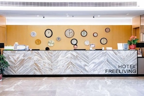 A hotel reception desk with a marble-patterned counter and multiple clocks on the wall.