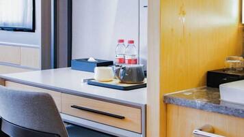 Una habitación de hotel compacta con kitchenette, un escritorio y silla, cama y ventana.