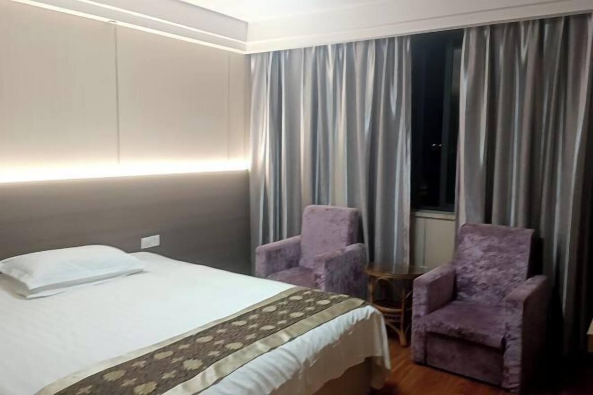 Habitación de hotel con cama, dos sillones, una mesita y una ventana con cortinas.