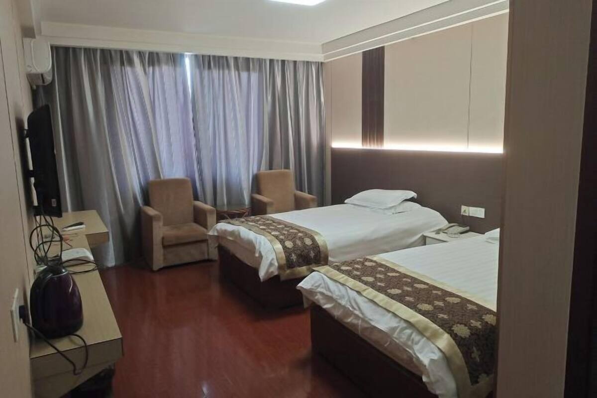 Habitación de hotel con dos camas, un escritorio, una silla y un ventanal con cortinas.