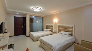 Habitación de hotel con dos camas, un escritorio con computadora, un televisor y un baño con puerta de vidrio.