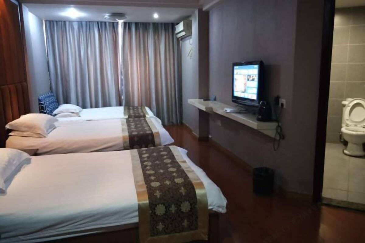 Habitación de hotel con dos camas, televisión, estante pequeño y un inodoro.