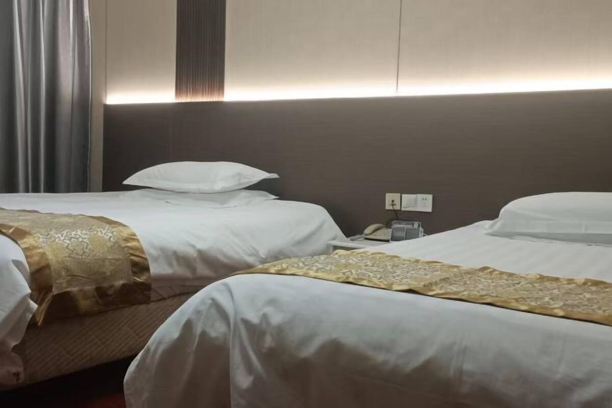 Habitación de hotel con dos camas, una mesita de noche, un teléfono y una lámpara fijada a la pared.