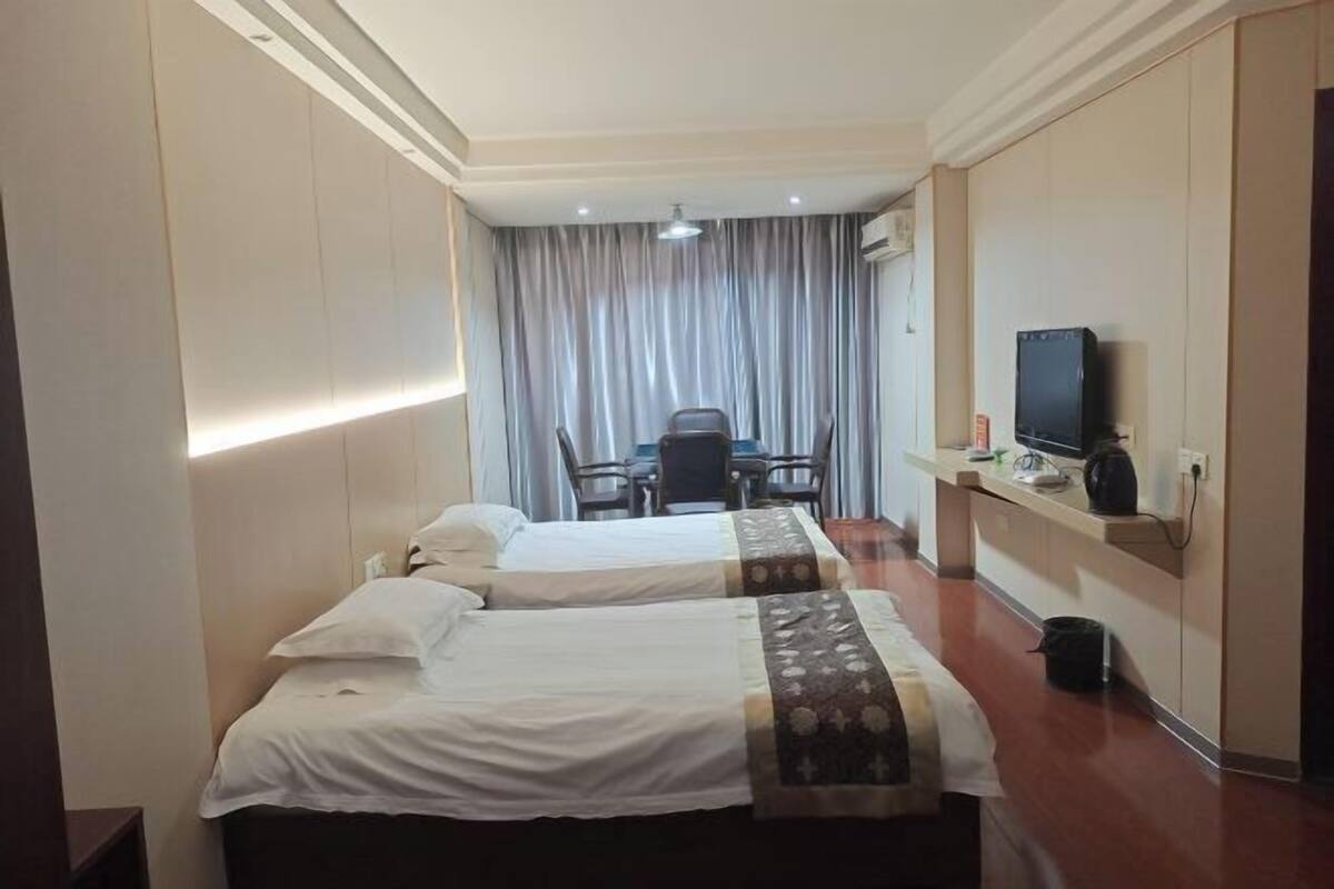 Habitación de hotel con dos camas, un escritorio, una silla, un televisor y una kitchenette pequeña.