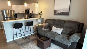 A modern kitchen with a central island, bar stools, a grey sofa, and a coffee table.