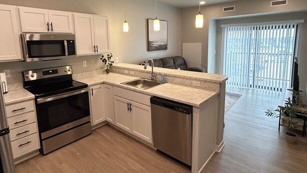 A modern kitchen with stainless steel appliances, white cabinetry, and a central island with a sink.
