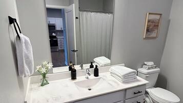 A bathroom with a white vanity, a sink, a mirror, a toilet, and a shower curtain.