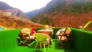 A dining area with a table and chairs, set against a backdrop of mountains and a clear sky. - Rahm Holiday Theme Hotel (Xiaojin)