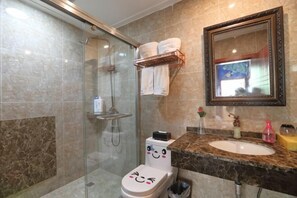 A bathroom with a glass shower enclosure, a toilet with a face decal, a sink with a marble countertop, and a mirror with a decorative frame. - Rahm Holiday Theme Hotel (Xiaojin)