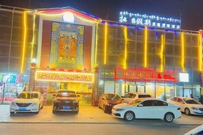 A hotel with a large illuminated sign, multiple parked cars, and a decorative wall. - Rahm Holiday Theme Hotel (Xiaojin)