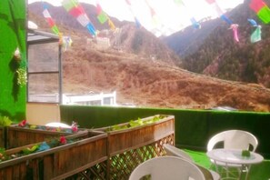 A balcony with a view of a hilly landscape, a white chair, and a small table. - Rahm Holiday Theme Hotel (Xiaojin)