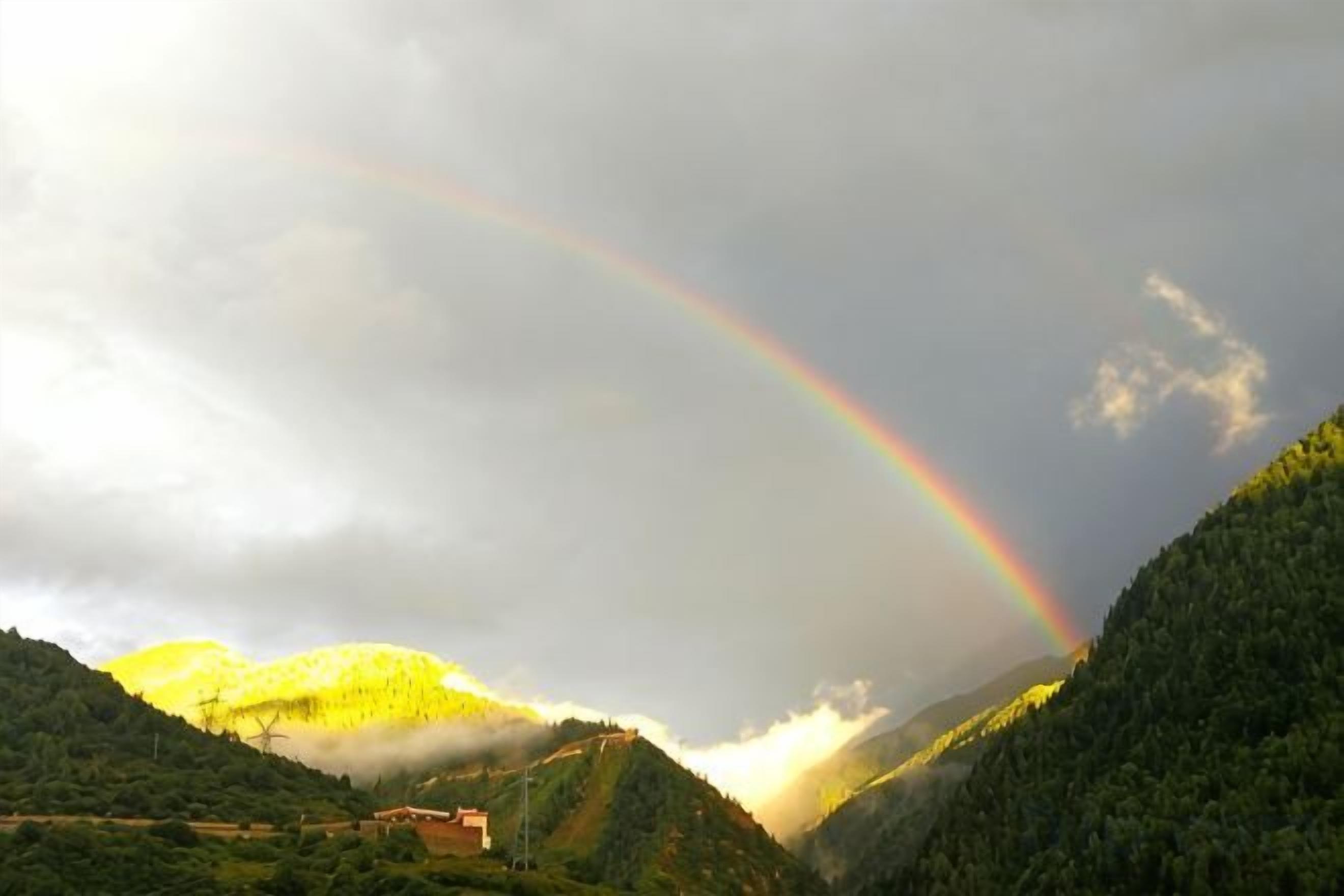 Un paysage de montagne avec un arc-en-ciel et un bâtiment situé sur une colline.