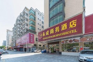 Un hotel con un letrero rojo llamativo, varios pisos y un estacionamiento frente a él.
