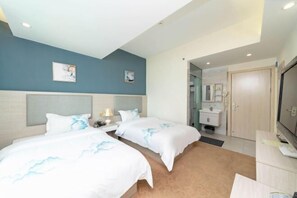 Habitación de hotel con dos camas, un escritorio, televisión y baño visible a través de una puerta abierta.