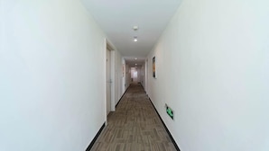 Un pasillo largo y estrecho con paredes blancas y piso alfombrado, que conduce a una puerta al final.
