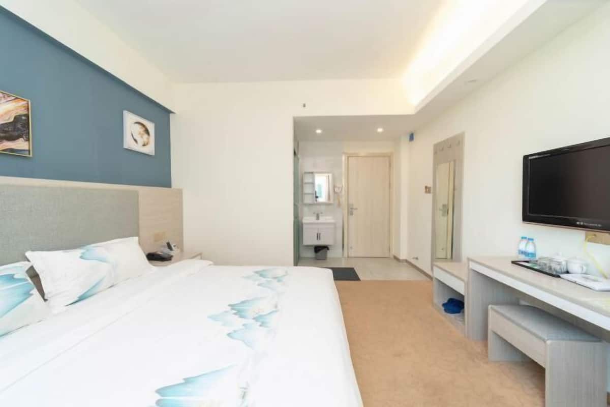 Habitación de hotel moderna con una cama grande, un escritorio, televisión y un baño visible al fondo.