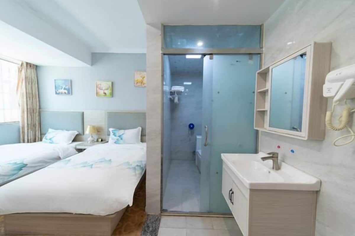 Habitación de hotel con dos camas, baño con espejo y secador de pelo, y ventana con cortinas.