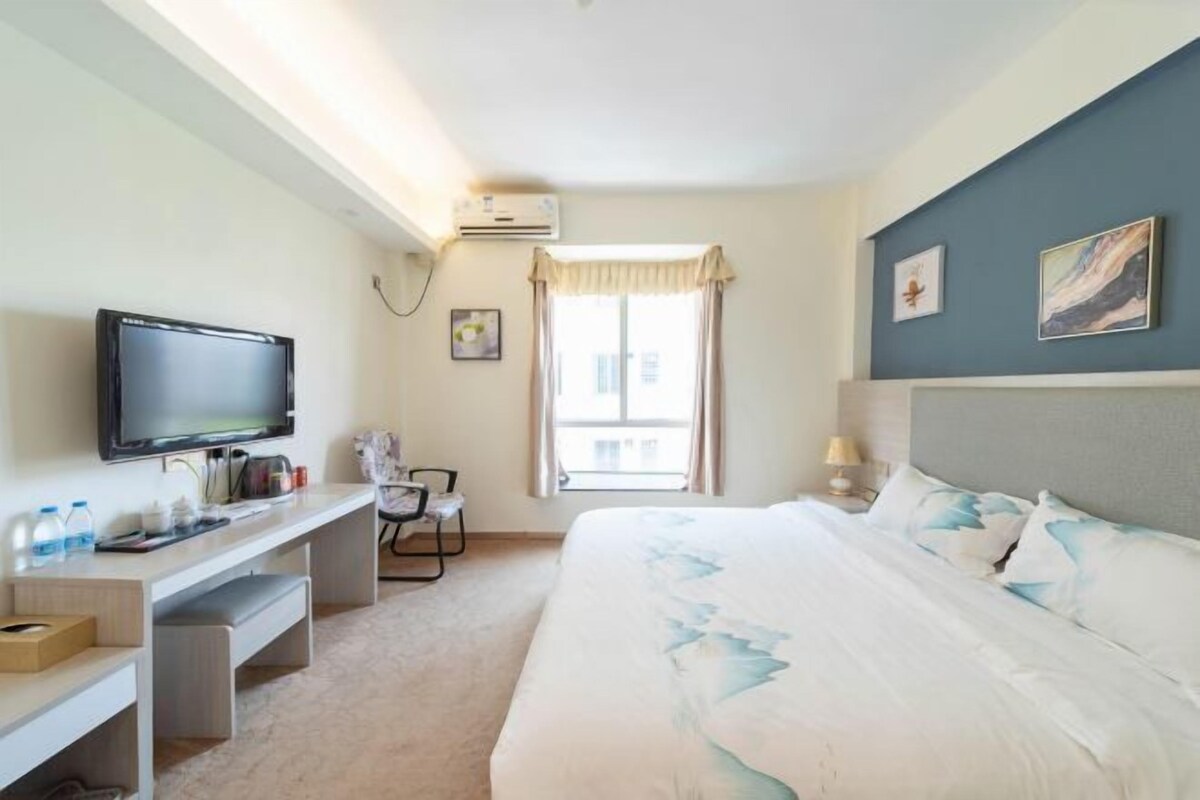 A hotel room with a bed, a desk, a television, a window with curtains, and artwork on the wall.