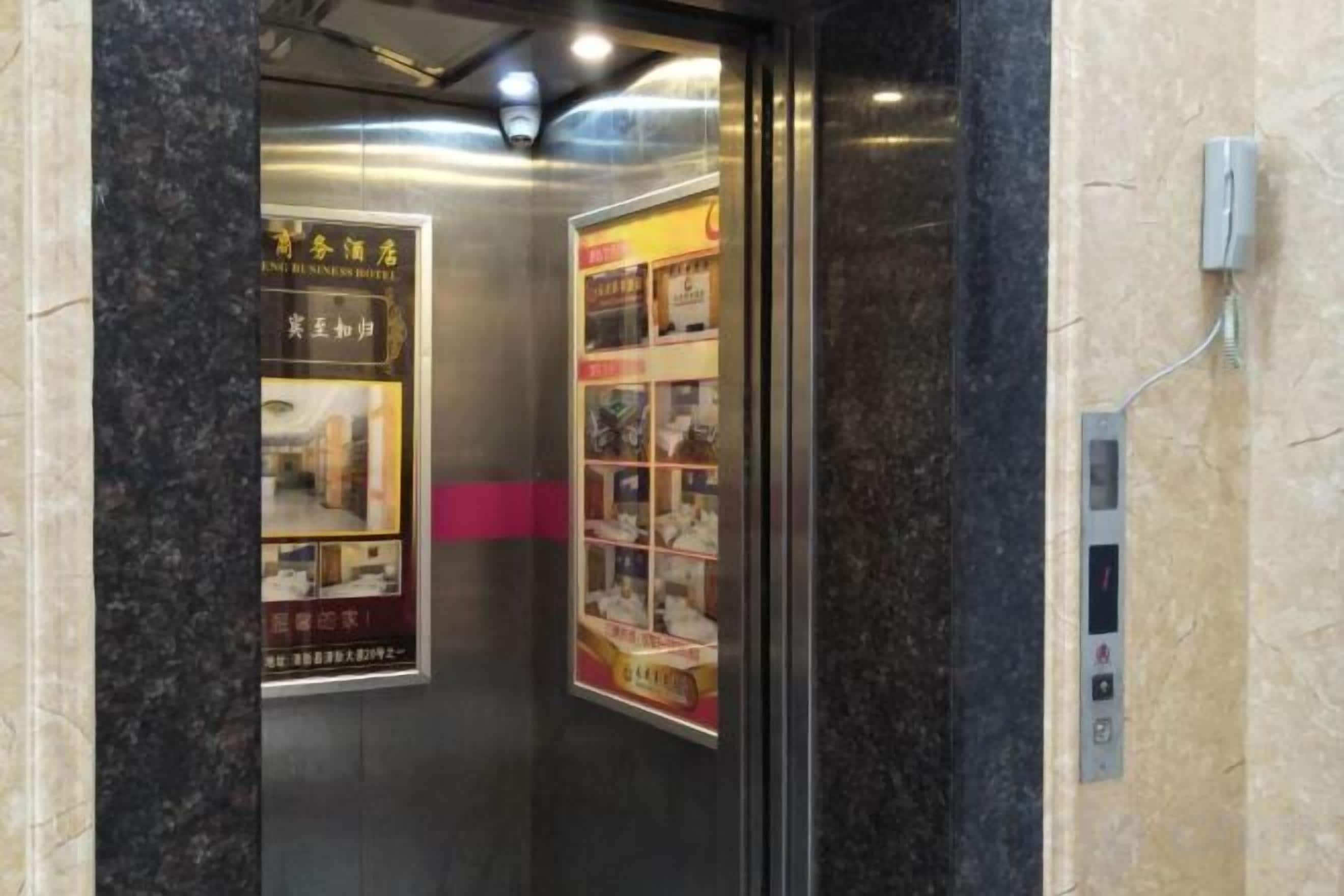 An elevator interior with a marble wall, a control panel, and two posters advertising a hotel.