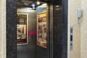 An elevator interior with a marble wall, a control panel, and two posters advertising a hotel.